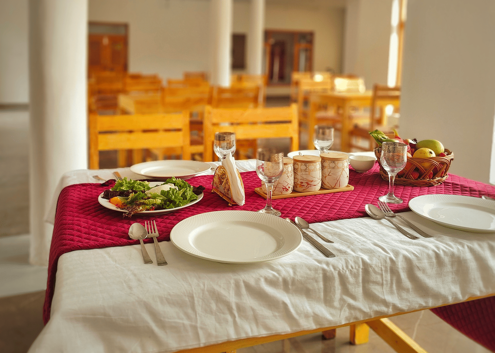 A set dining table with a red runner and white crockery in a bright, airy restaurant at Indus Serenity Retreat.