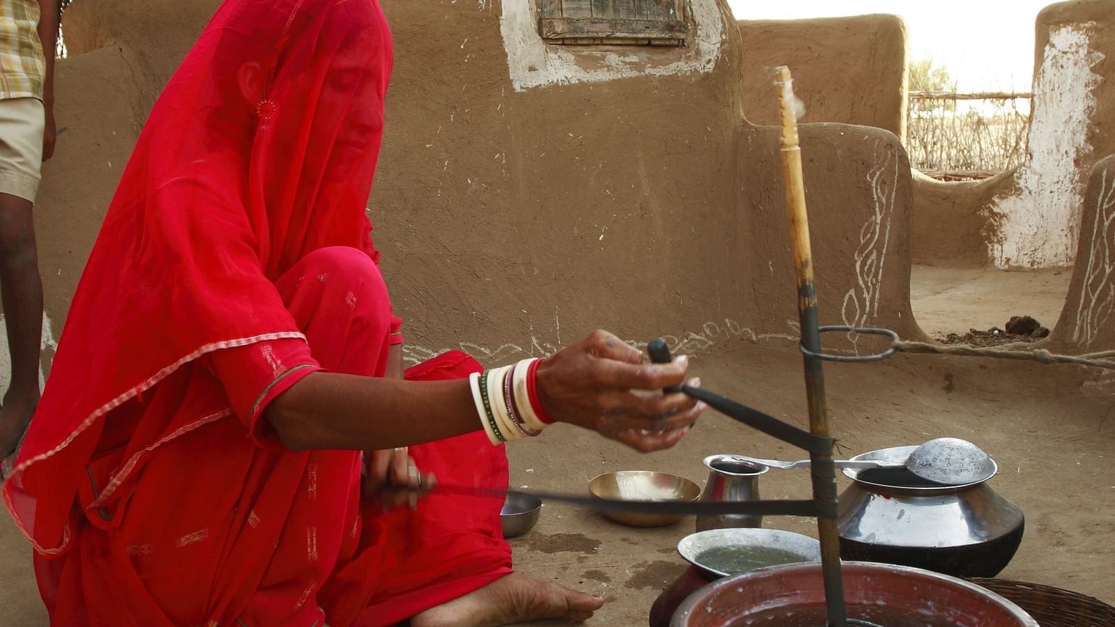 A lady cooking food in a village with her mud house next to her