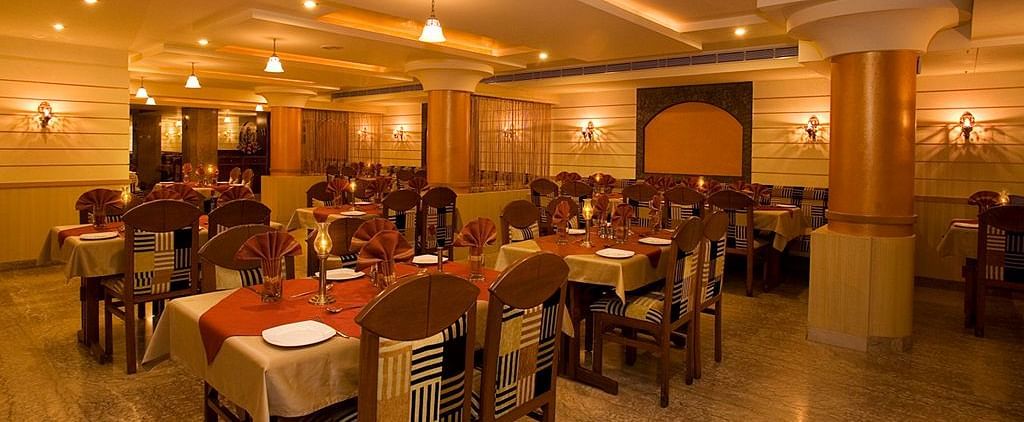 An image of a restaurant with several sets of chairs and table, and at one corner there is a reception desk - Hotel Pai Comforts JP Nagar Bangalore