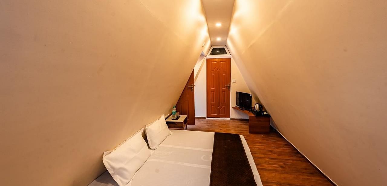 A hotel room with angled walls creating a narrow appearance, a bed, and a television visible at the far end.