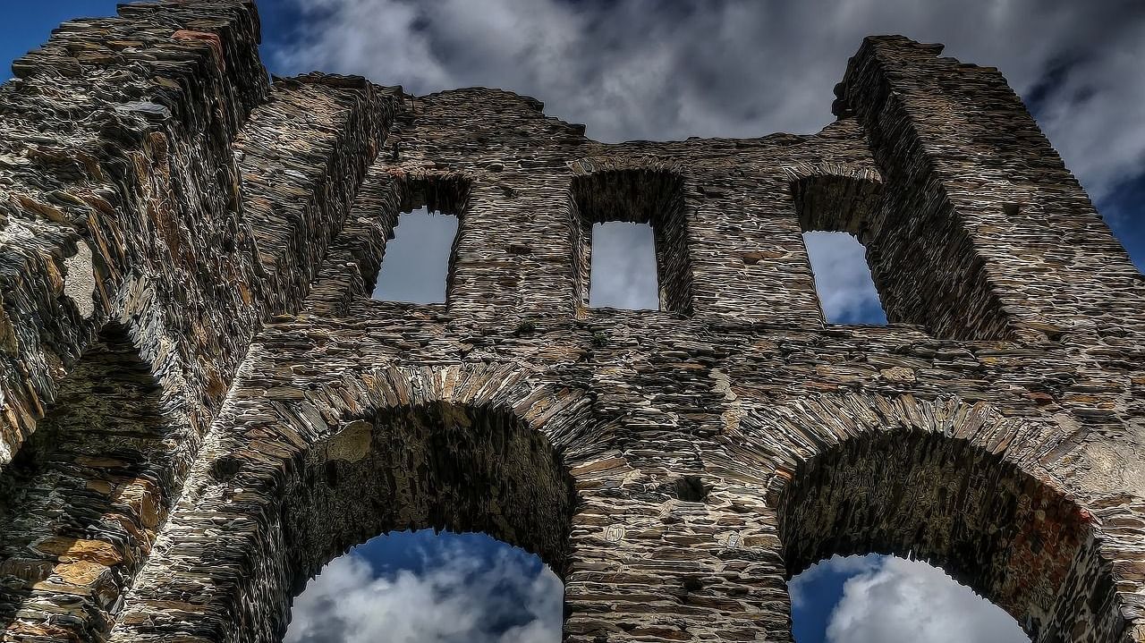 A view from below of of fort in ruins with white clouds on blue sky in the background.
