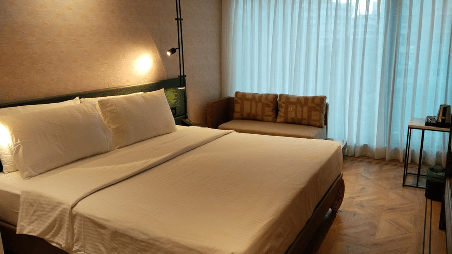 The Deluxe Room at Regency Hotel, Mumbai, featuring a neatly-made bed, a seating area, and sheer curtains.
