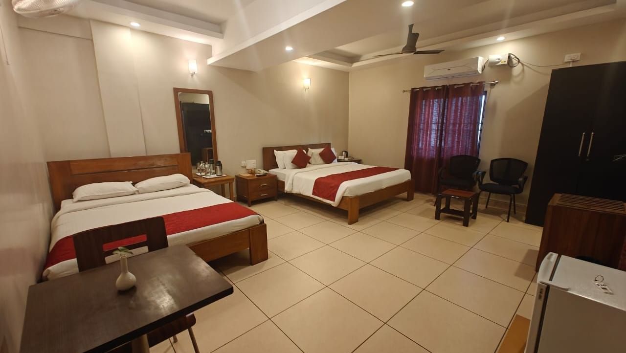 Bright Deluxe Family Room at Woodstock Resorts, Coorg with twin beds, dining table, TV, and contemporary furnishings.