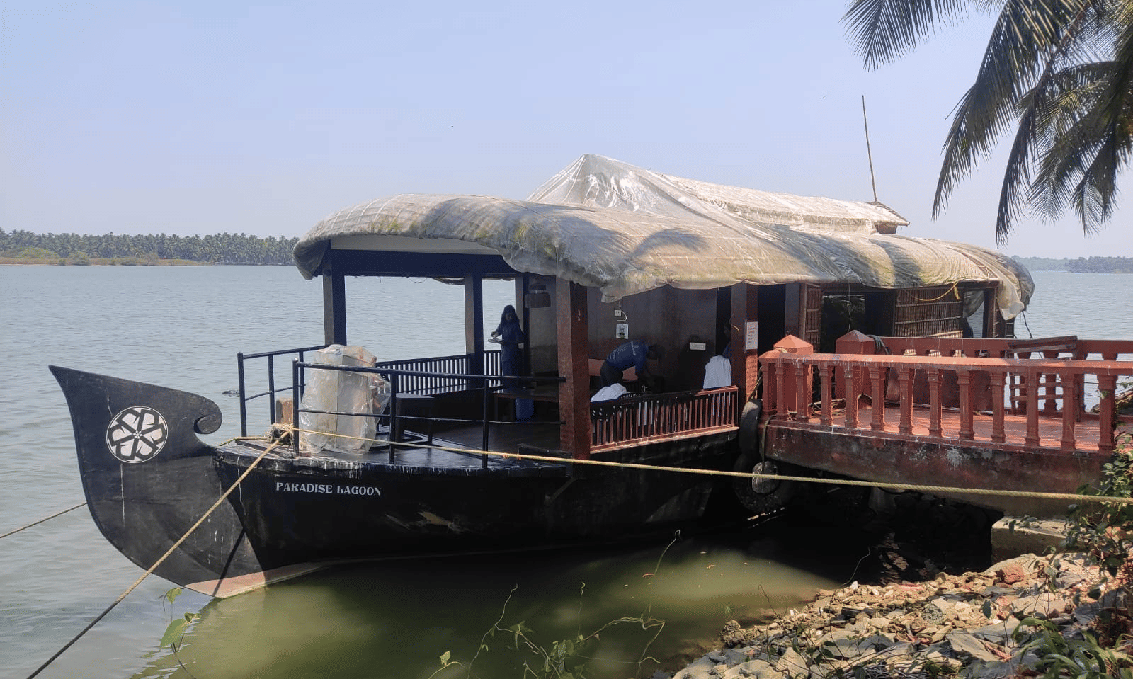 Houseboat with canopy roof anchored by the water at Paradise Lagoon Resort, Udupi.
