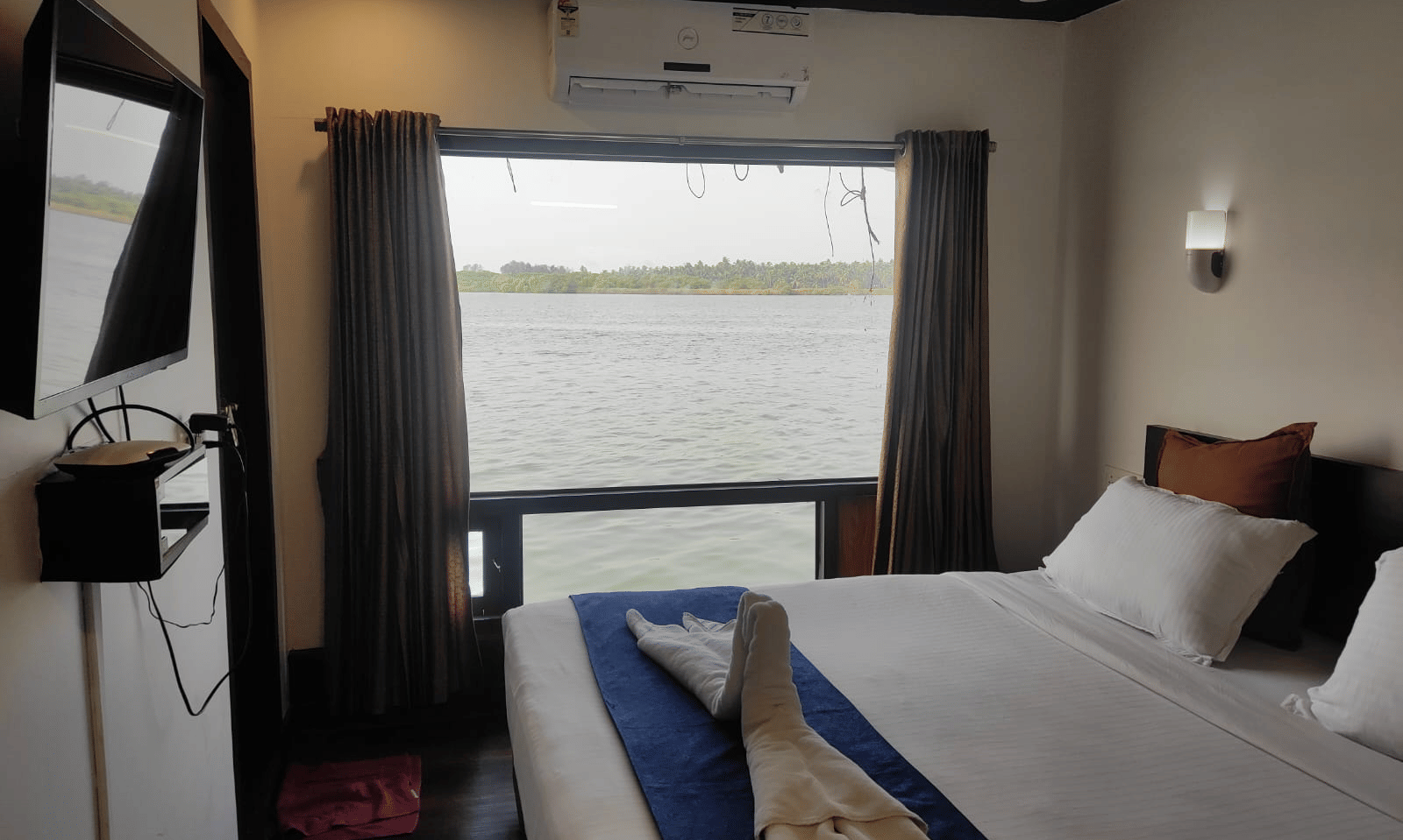 Bedroom with a queen bed, curtains, and window overlooking the water at Paradise Lagoon Resort, Udupi.