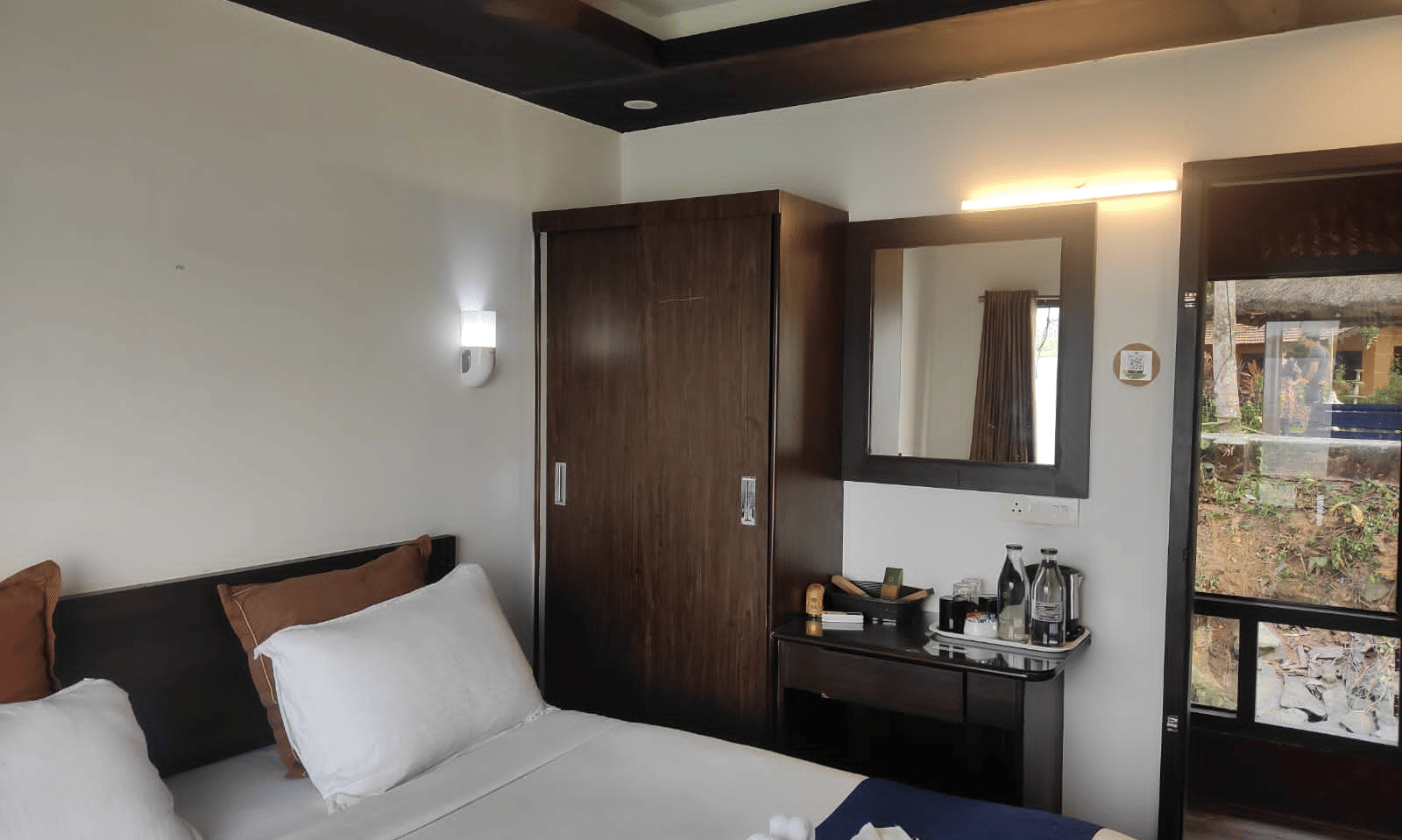 Bedroom with a queen bed, mirror, and wall-mounted light at Paradise Lagoon Resort, Udupi.