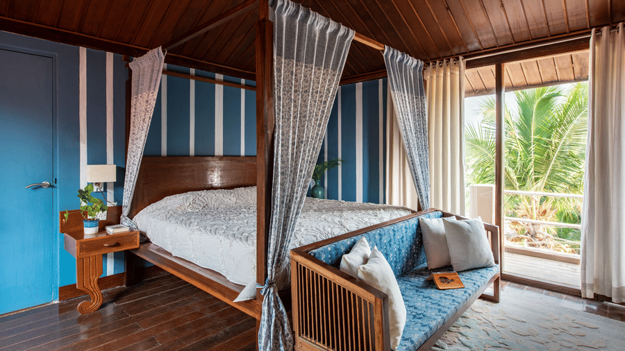 Four poster king size bed with white canopy curtains in a wood-panelled room overlooking greenery.