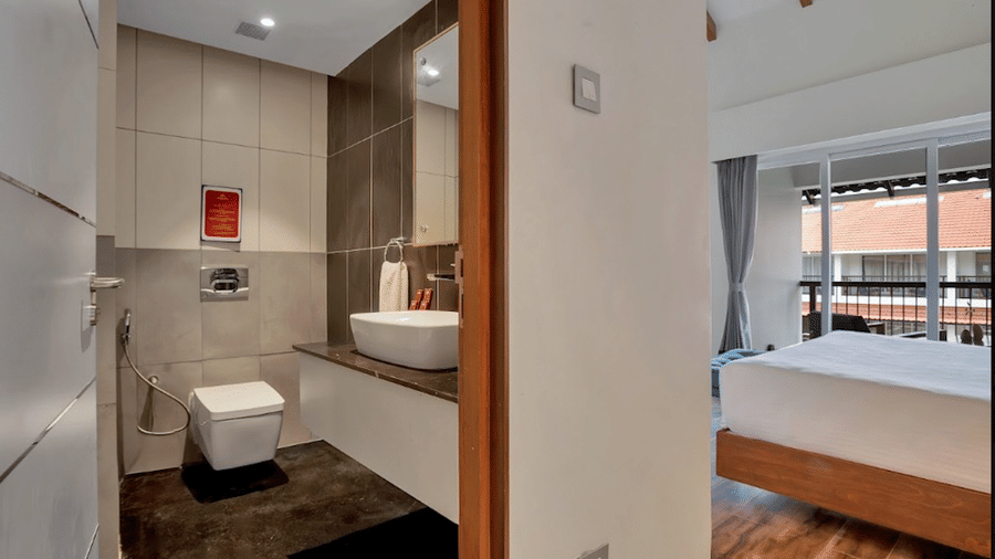 Bathroom inside Suite at Mango Hill, Velankanni with a sink, mirror, toilet, and doorway to the bedroom.