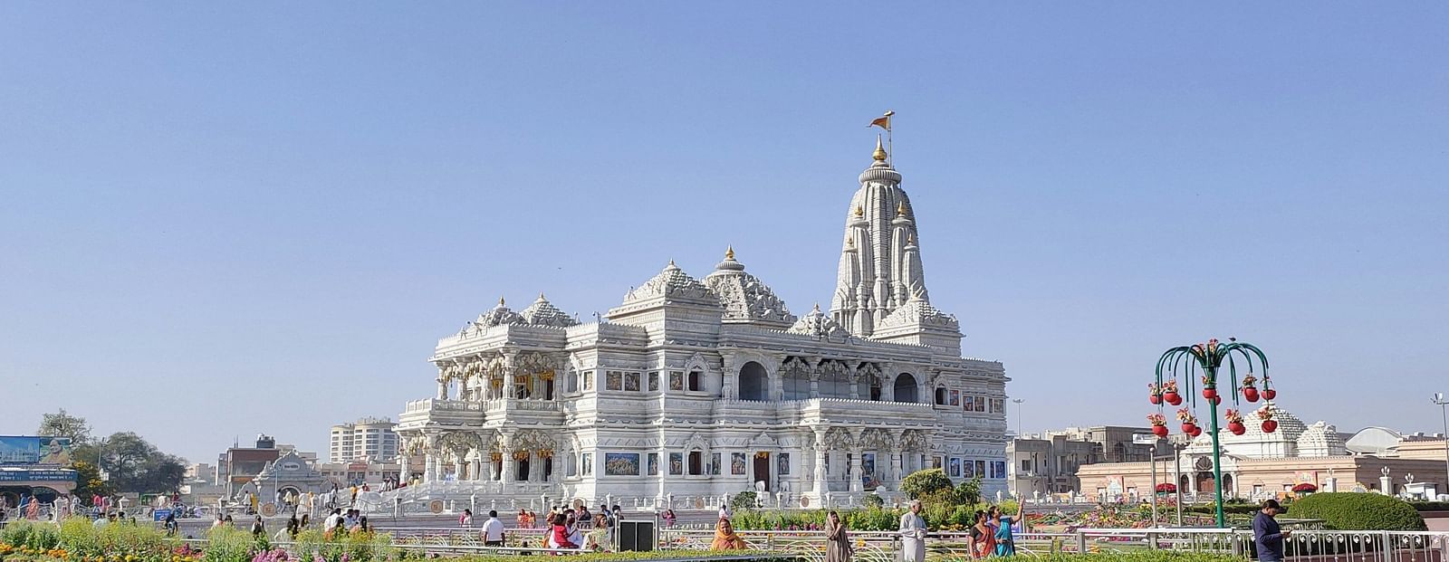 A facade of Prem Mandir in Vrindavan during the day time as devotees are strolling around premises embellished with flora and fauna