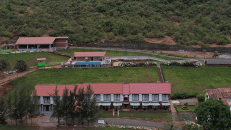 A red-roofed building and a large lawn at the base of a hill.