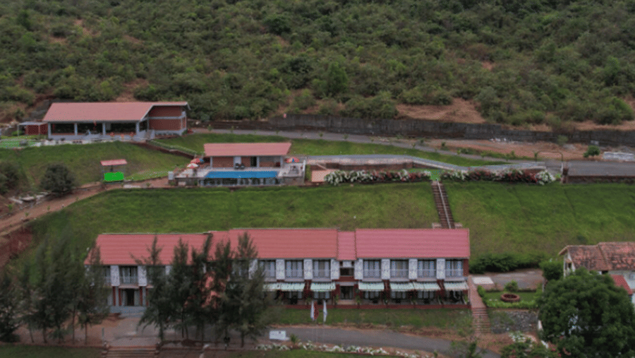A red-roofed building and a large lawn at the base of a green hill.