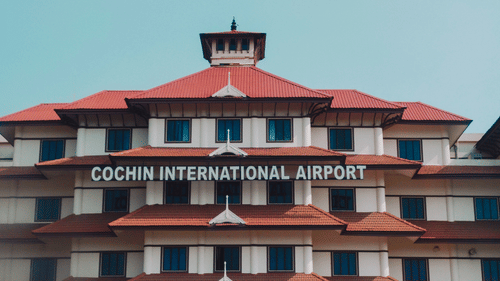 Cochin International Airport terminal building with distinctive red tiled roofs, white facade and central tower under a clear blue sky