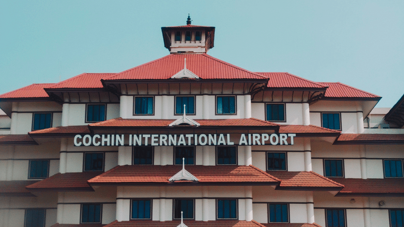 Cochin International Airport terminal building with distinctive red tiled roofs, white facade and central tower under a clear blue sky
