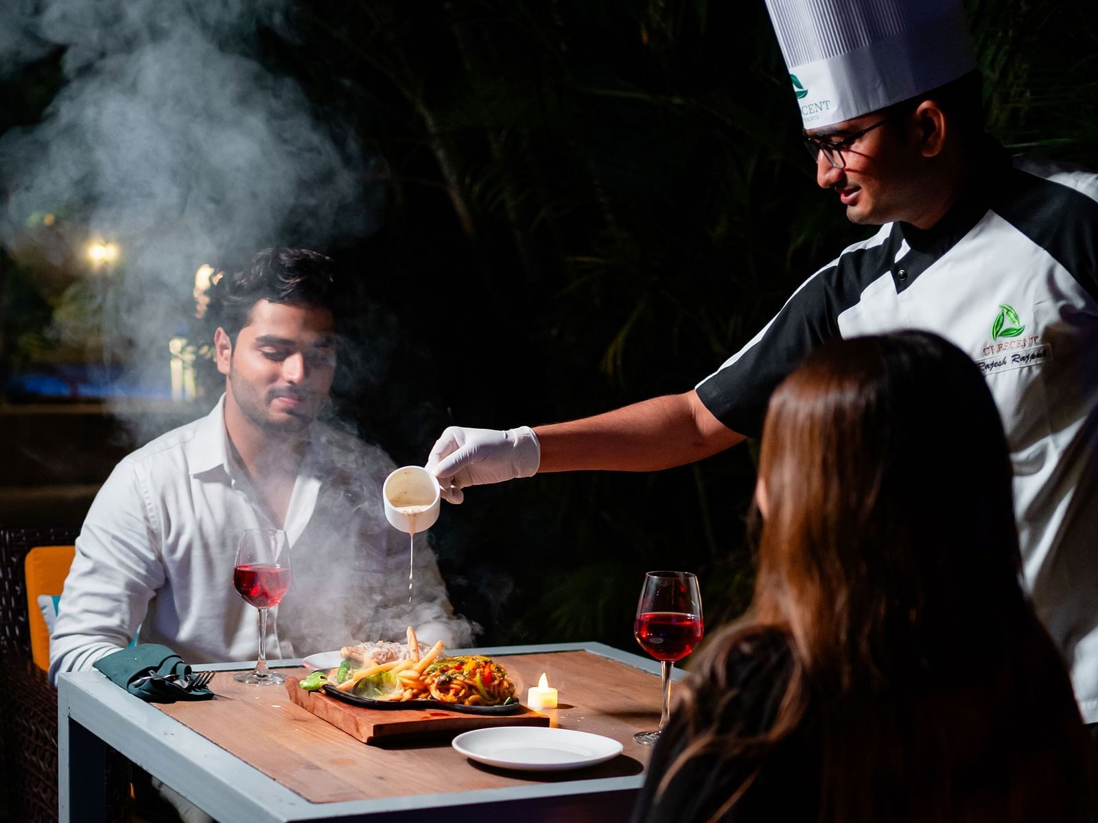 A couple being served by a chef at the poolside, relishing a charming dining experience at Crescent Spa & Resort, Indore