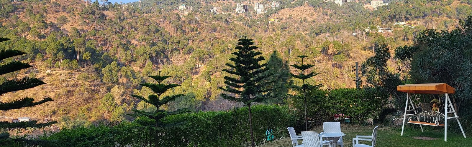 A scenic outdoor garden with a swing, white chairs, and mountain views at Dagshai Manor Kasauli - Inde Hotels.