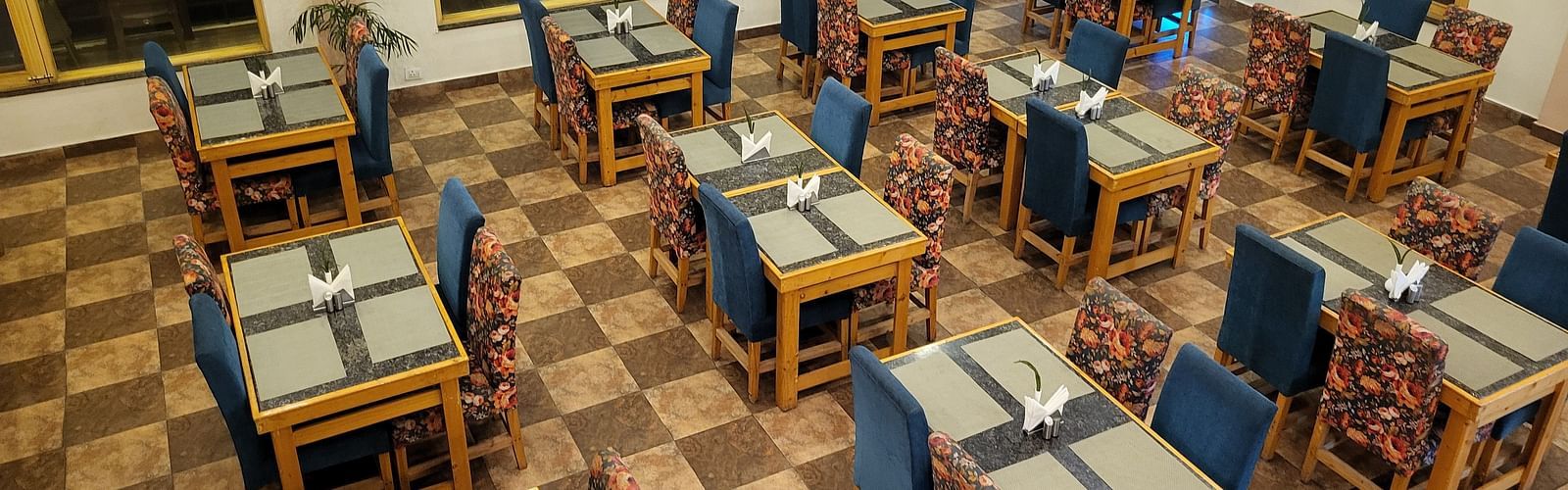 A spacious dining area with neatly arranged tables, wooden chairs, and a warm, inviting ambience at Dagshai Manor Kasauli - Inde Hotels