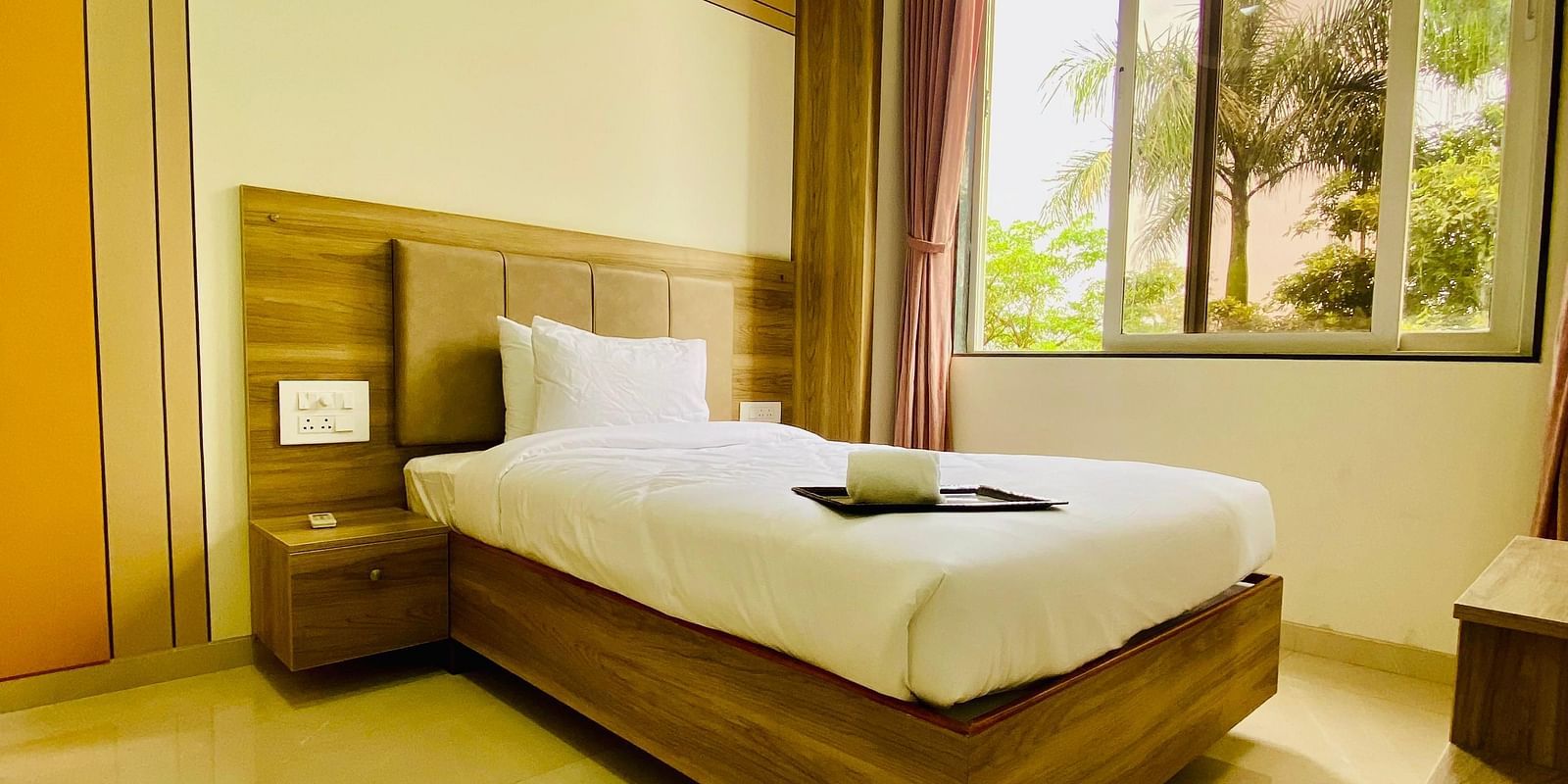A bright hotel room featuring a neatly made bed, large windows, and a peaceful view of the outdoors.