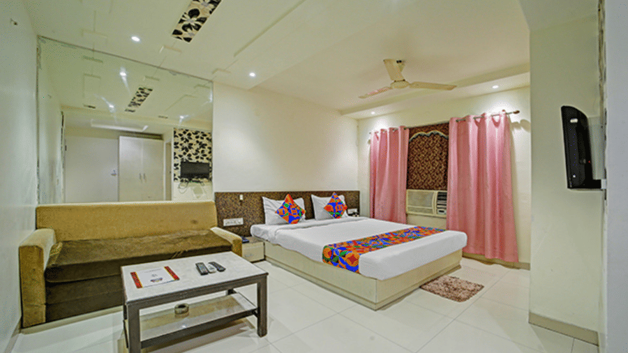 Large room with two beds, coffee table, wall art, TV and pink curtains at Hotel Maurya, Bhopal.