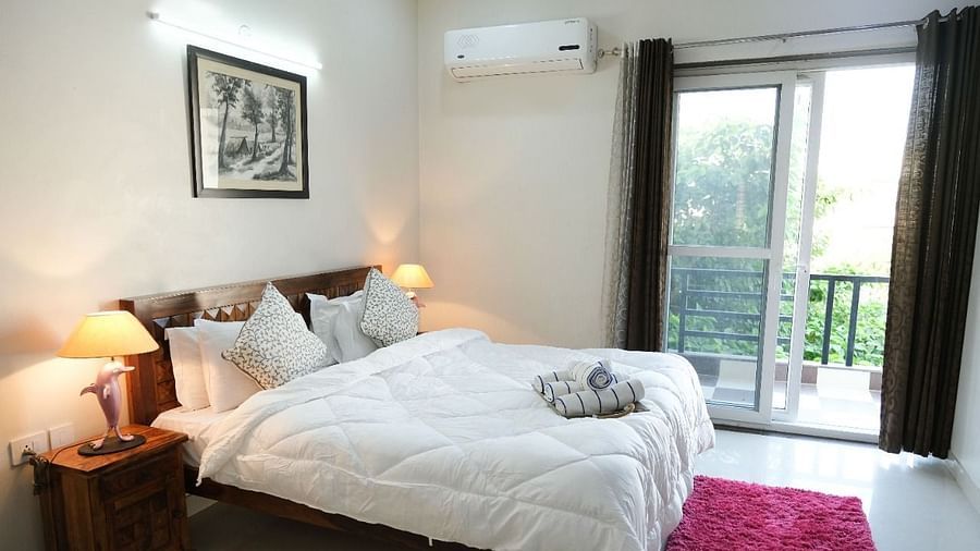 An image of a bedroom featuring a bed, a bedside table with lamp, anda a glass door leading to the balcony - LIme Tree 3BHK Serviced Apartments Near Medanta HospitalAn image of a bedroom featuring a bed, a bedside table with lamp, anda a glass door leading
