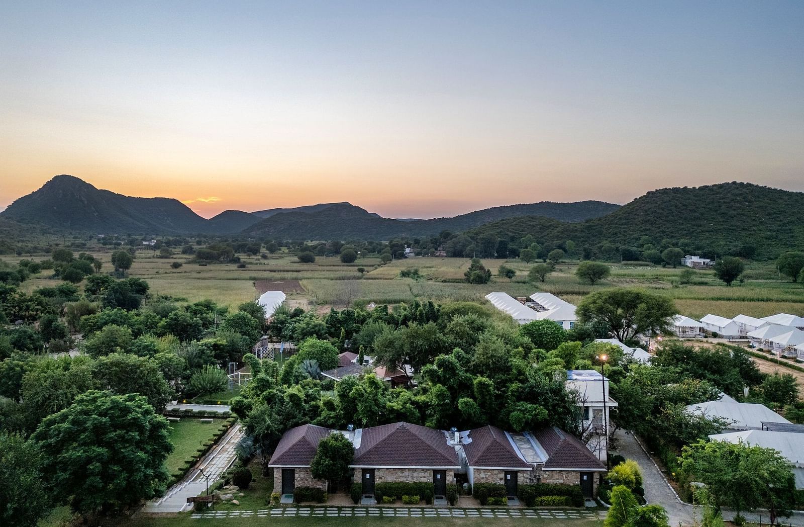 Aerial view of Valley by Grassfield, surrounded by lush greenery with mountains in the background.