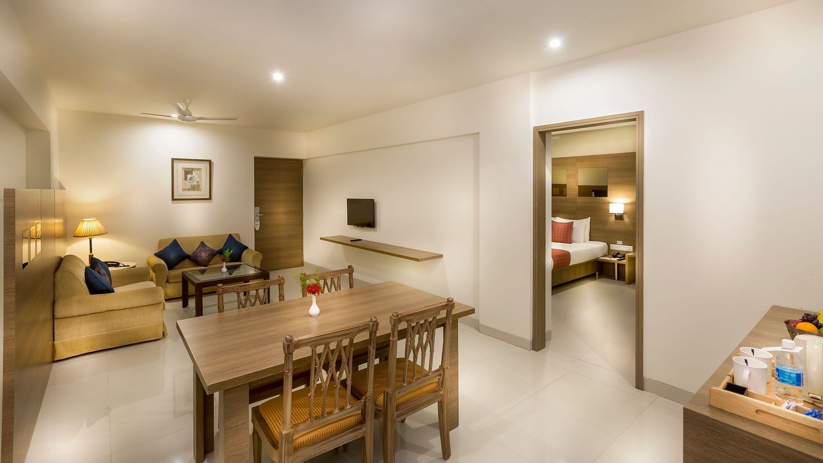 An image of the living room of a Suite with wooden dining table and chairs and comfortable sofas at Regency Tiruttani by GRT Hotels.