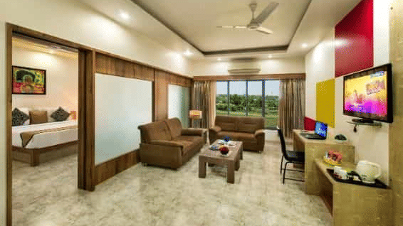 A spacious room including a seating area with sofas, a television, and large windows - Lion Lords Inn Rajula