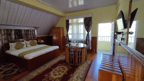 A double bed room with a carpet, table, windows and door open