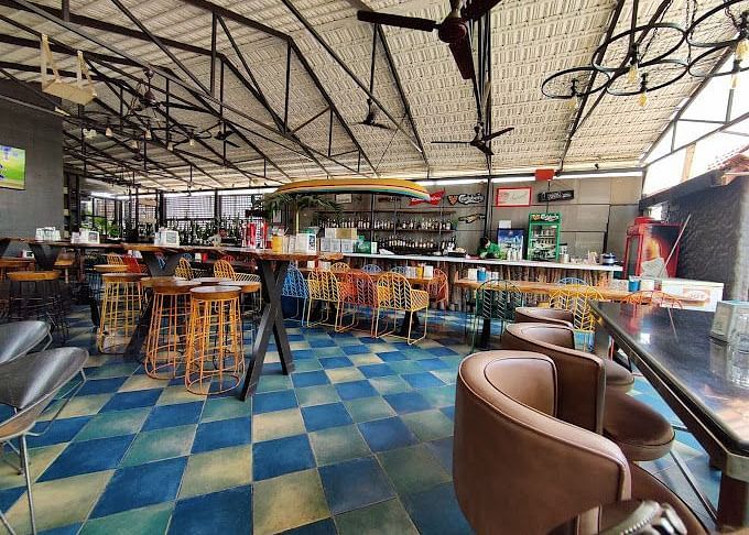 Spacious indoor restaurant with high ceilings, exposed beams, colorful chairs, and a checkered blue and white floor | Astra Hotels and Suites Kadubeesanahalli