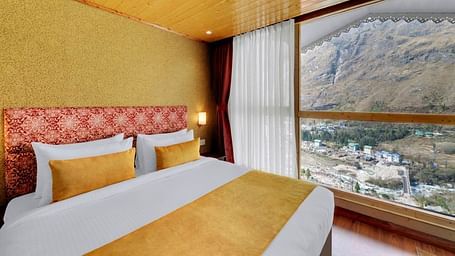 Image of a room at our hotel with wooden ceiling and flooring featuring a bed beside an expansive window overlooking the mountains  | Yashshree Lachung