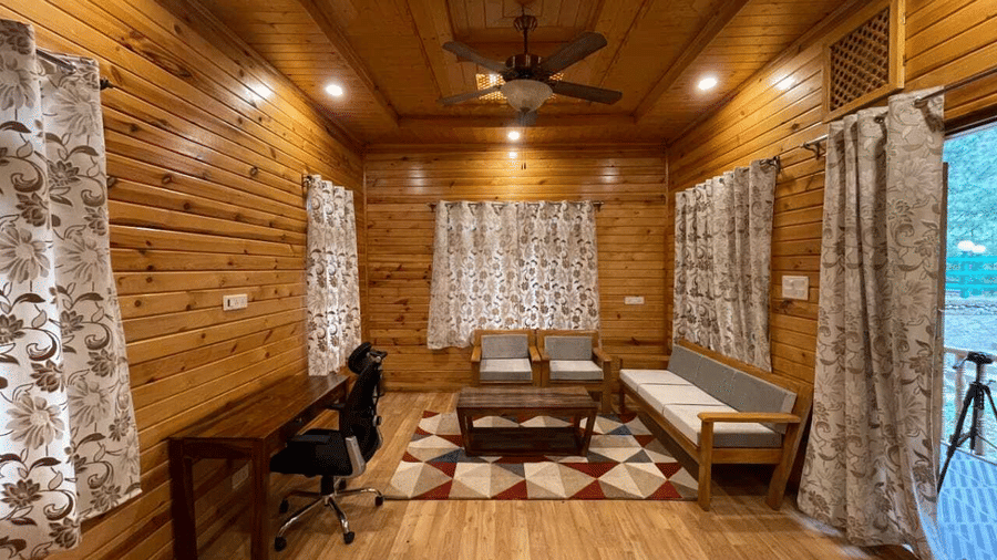 A living room at Dawat e Drung by FrozenFall Resort, Drung, Tangmarg, featuring a sofa, a coffee table, a writing desk with a chair and curtains.