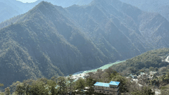 Aerial view of Rishikesh nestled in the Himalayan foothills, with the Ganges River winding through a verdant valley surrounded by layered mountain ridges.