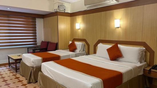 Guest room at Hotel Swagath, Bangalore featuring a double bed with white linens, orange runner, and modern wooden interiors.