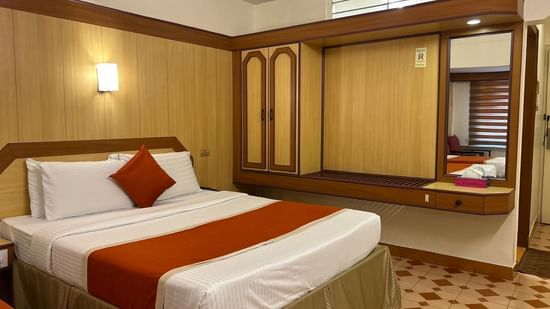Single occupancy room at Hotel Swagath, Bangalore with a cozy bed, wooden wardrobe, and bedside lamp.