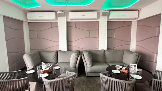 Modern indoor lounge area featuring comfortable grey sofas, armchairs, and distinct green ceiling lighting.