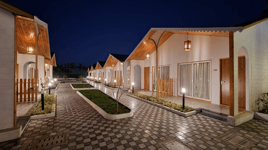 A view of the cobbled walkway with manicured lawn in the centre and Cottages on either side, as seen during the night at VITS Daman Devka Beach, the hotel provides the best accommodation in Daman.
