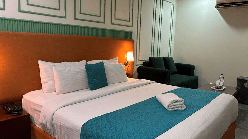 An interior view of a hotel room featuring a bed with pillows,  a sofa and decorative wall paneling - Asian Suites IFFCO Chowk Metro Station, Gurgaon. 