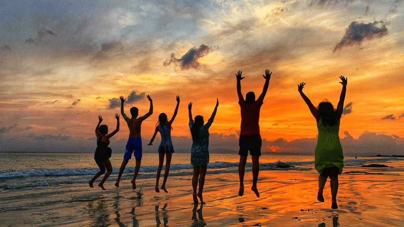 A group of people on a beach in Havelock Island, jumping and posing for a picture while looking at the sunset in the distance. Barefoot at Havelock provides the best offers in Havelock Island.