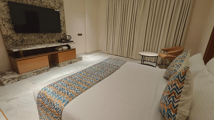Family room showing a bed positioned opposite a television console, with decorative wall panels and soft curtains. The layout ensures clear sightlines, comfortable seating space, and a practical arrangement for group stays.