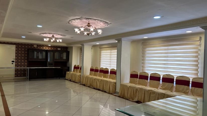 Banquet hall at Hotel Swagath, Bangalore with rows of red chairs, glossy flooring, and elegant ceiling lights.