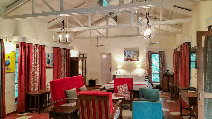 Inviting indoor lounge with wooden chairs upholstered seating high sloped ceiling and large windows creating a relaxed social space at Neemrana’s Glasshouse on The Ganges.