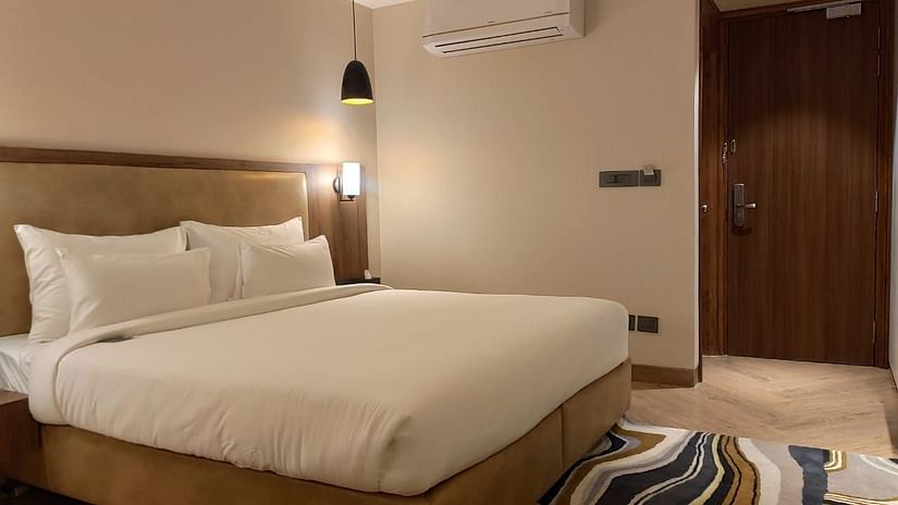 A plush bed in a warm-lit room with a carpet underneath and an AC on the top of the wall