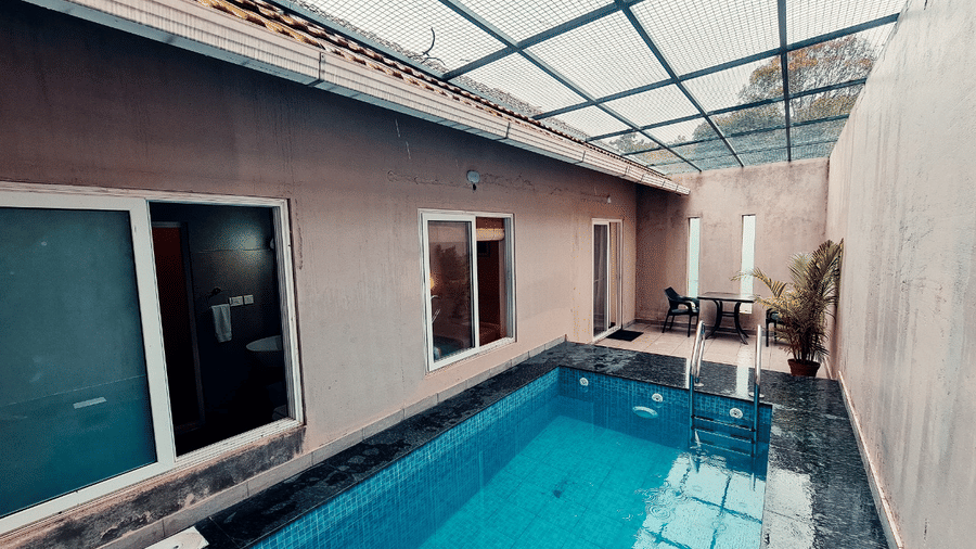 An indoor pool with a glass roof is adjacent to a building exterior, offering a bright and modern space.- Abad Brookside Lakkidi, Wayanad