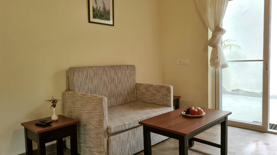 A living room features a sofa, table, and artwork on the wall, creating a cosy space.- Abad Brookside Lakkidi, Wayanad