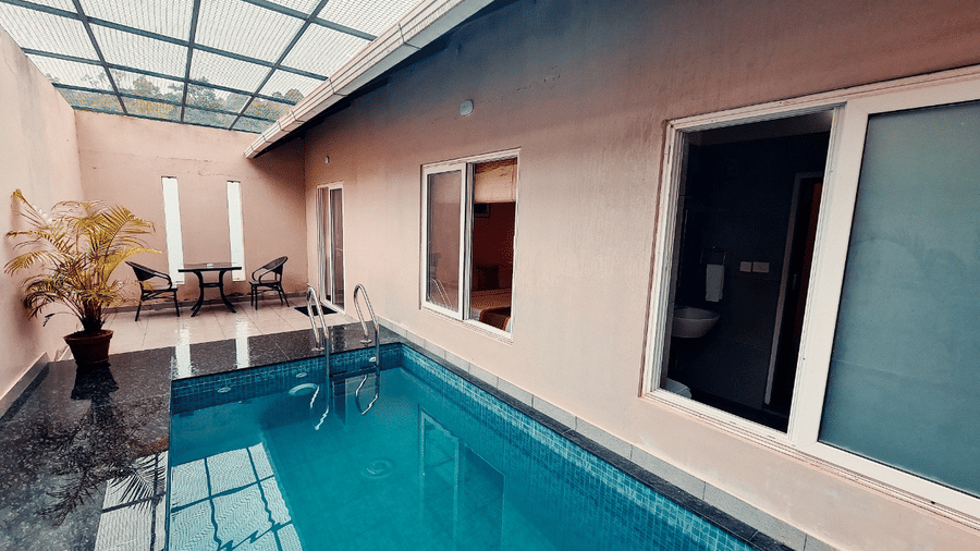 An indoor pool with a glass roof is adjacent to a building exterior, offering a bright and modern space.- Abad Brookside Lakkidi, Wayanad