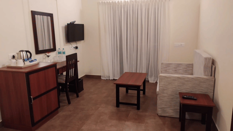 A room features a dresser, mirror, and stool, creating a simple space.- Abad Brookside Lakkidi, Wayanad