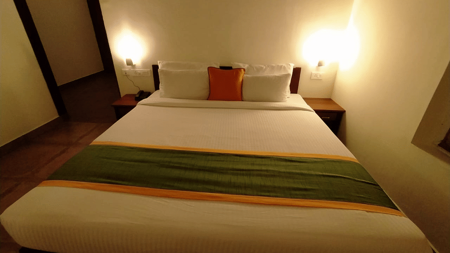 A bedroom features a made bed with a green accent and side lamps, offering a comfortable space.- Abad Brookside Lakkidi, Wayanad