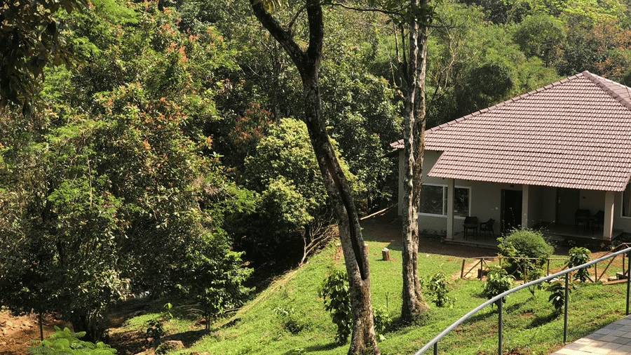 A hillside cottage surrounded by greenery, with a railing along the pathway.- Abad Brookside Lakkidi, Wayanad