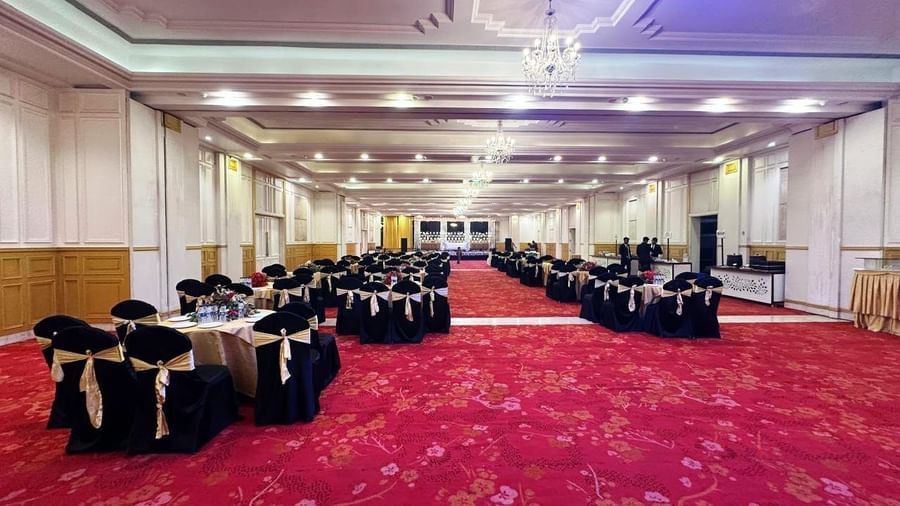  A wide view of a spacious Amer Greens banquet hall with a red and gold floral carpet, set with round tables draped in black and gold linen for an event.