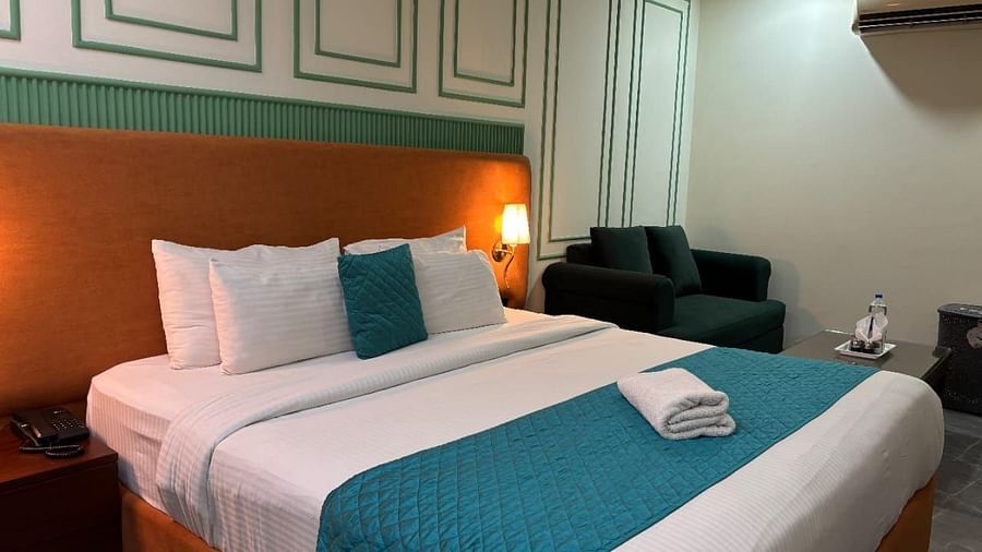An interior view of a hotel room featuring a bed with pillows,  a sofa and decorative wall paneling - Asian Suites IFFCO Chowk Metro Station, Gurgaon. 