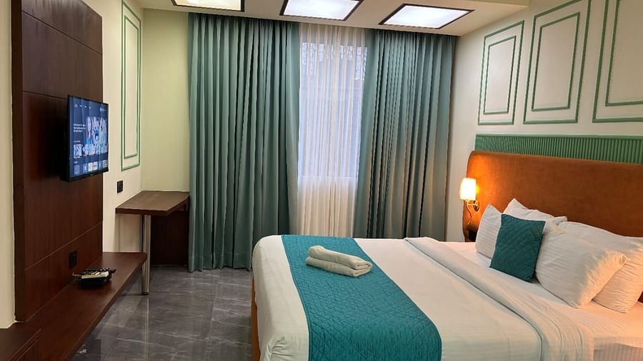 An interior view of a hotel room featuring a neatly made bed with pillows , a television and a window with curtains -  Asian Suites IFFCO Chowk Metro Station, Gurgaon.